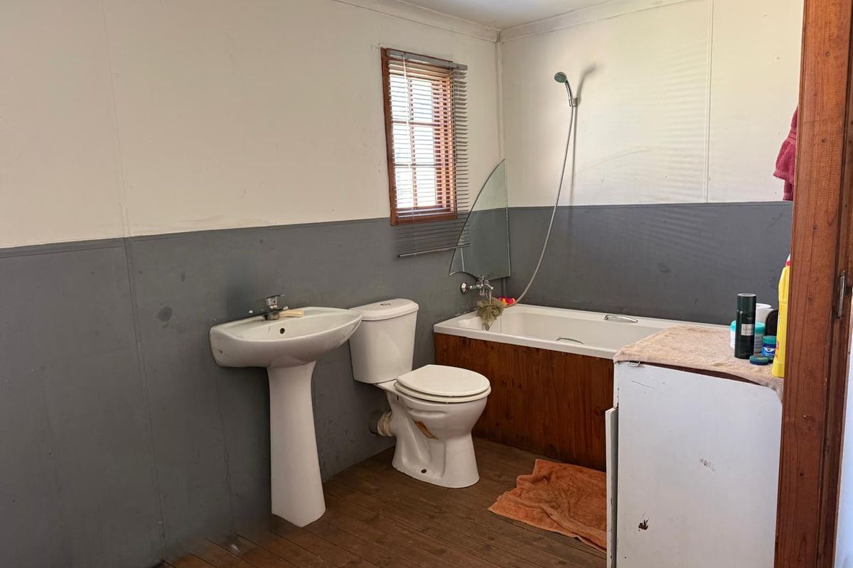 A functional bathroom featuring a pedestal basin, toilet, and bathtub with a handheld shower attachment, requiring cosmetic updates to finishes and wall surfaces.