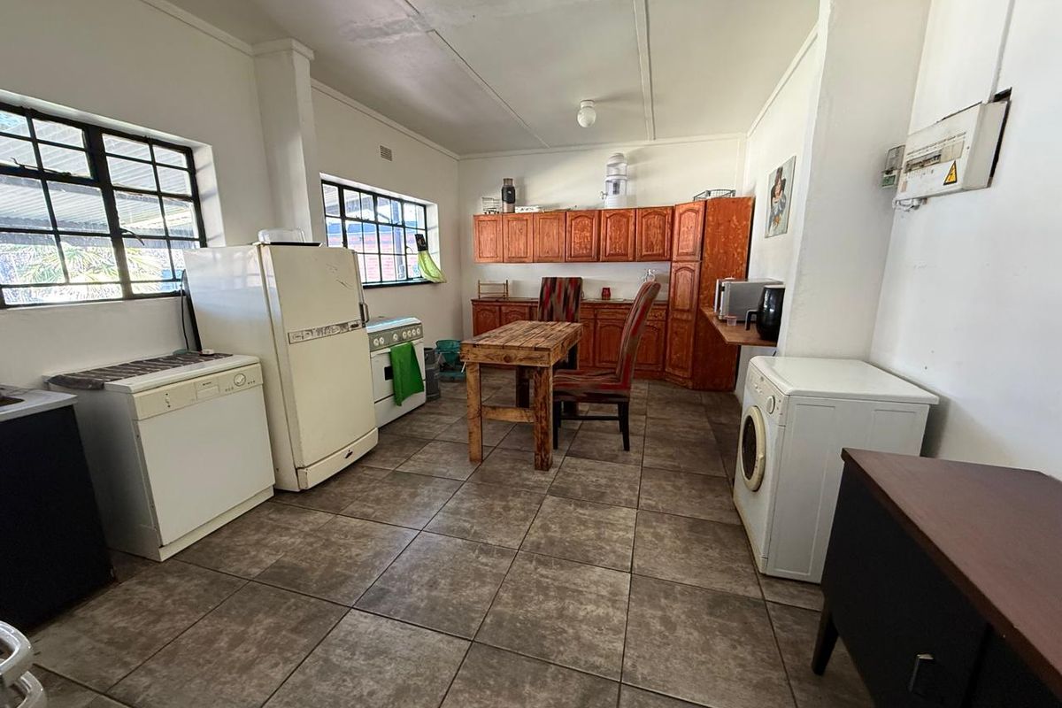 A functional kitchen space featuring wooden cabinetry, tiled flooring, and large steel-framed windows, offering a practical layout with potential for modern updates.