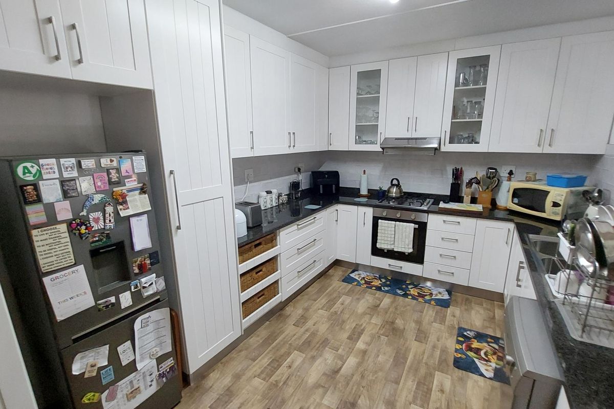 A well-maintained kitchen featuring white shaker-style cabinetry, dark granite countertops, built-in oven with gas hob, and durable laminate flooring.