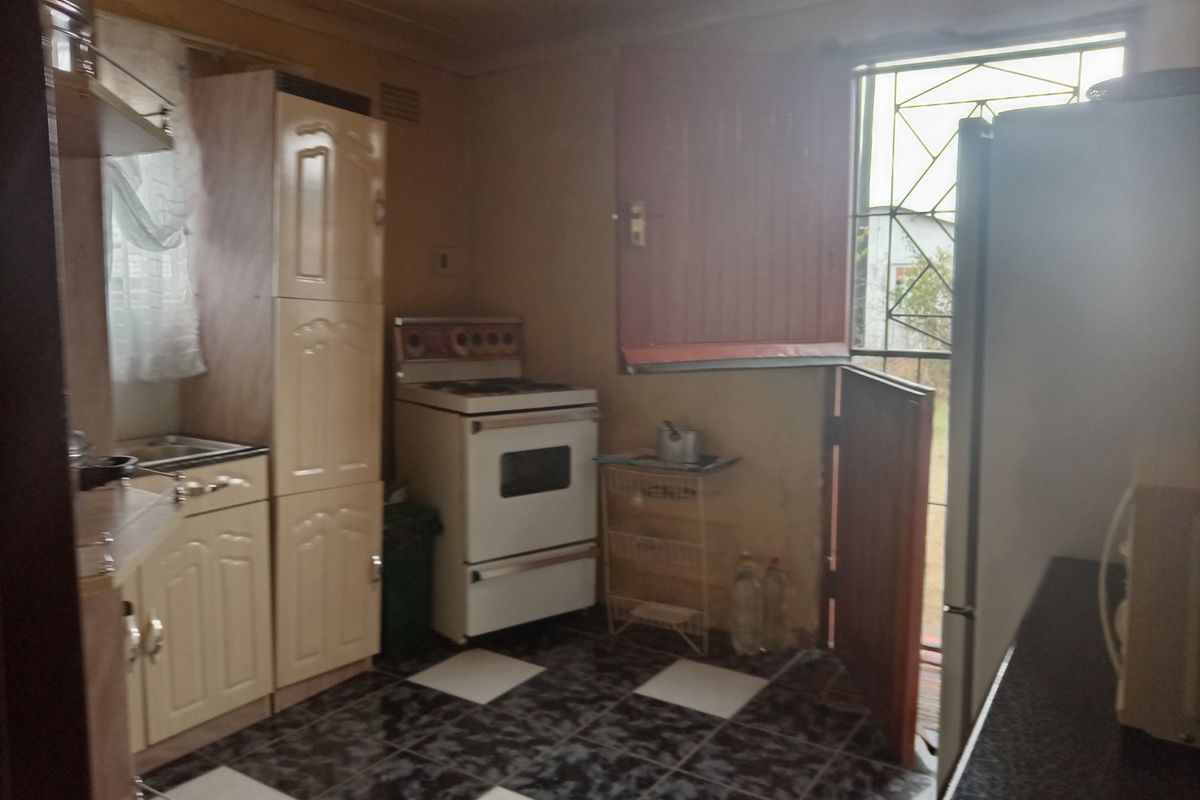 A dated kitchen featuring built-in cabinetry, a freestanding stove, and tiled flooring with direct access to the exterior via a security gate.