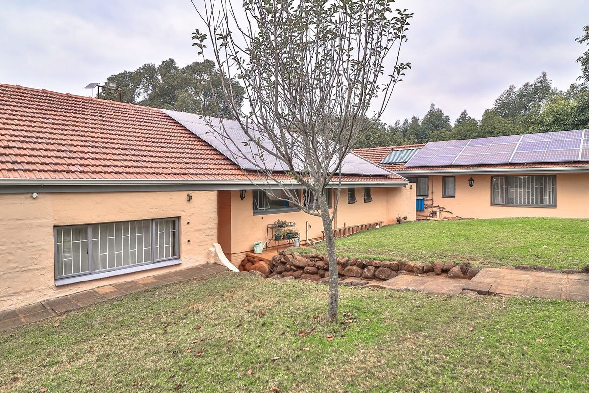 Rear view of the house featuring terracotta tiled roofing, installed solar panels, stone retaining wall, and a landscaped garden area.