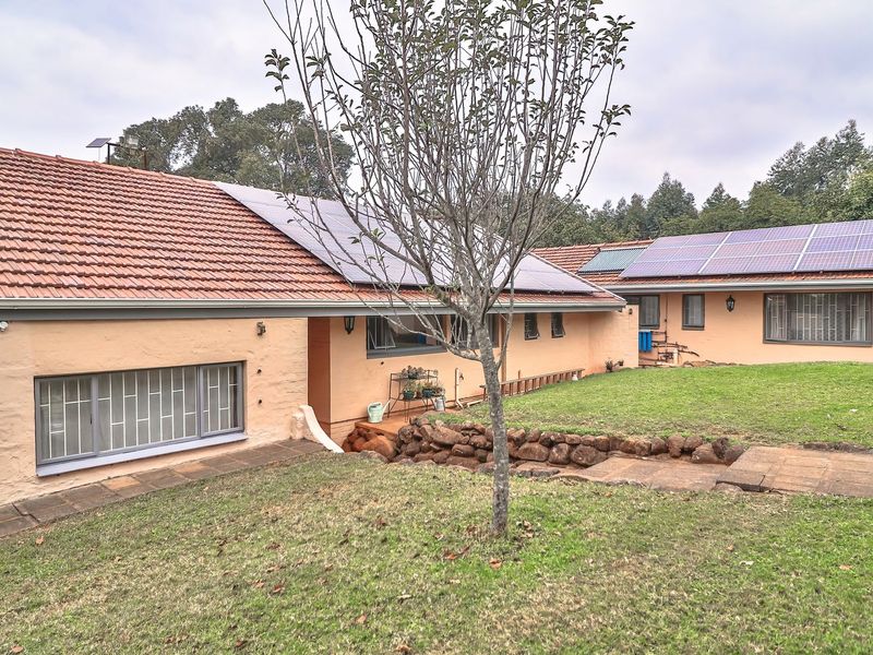Rear view of the house featuring terracotta tiled roofing, installed solar panels, stone retaining wall, and a landscaped garden area.