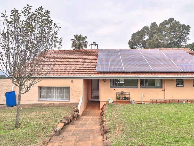 Rear view of a single-story house featuring a tiled roof with integrated solar panels, a stone-edged pathway, and a surrounding garden area.