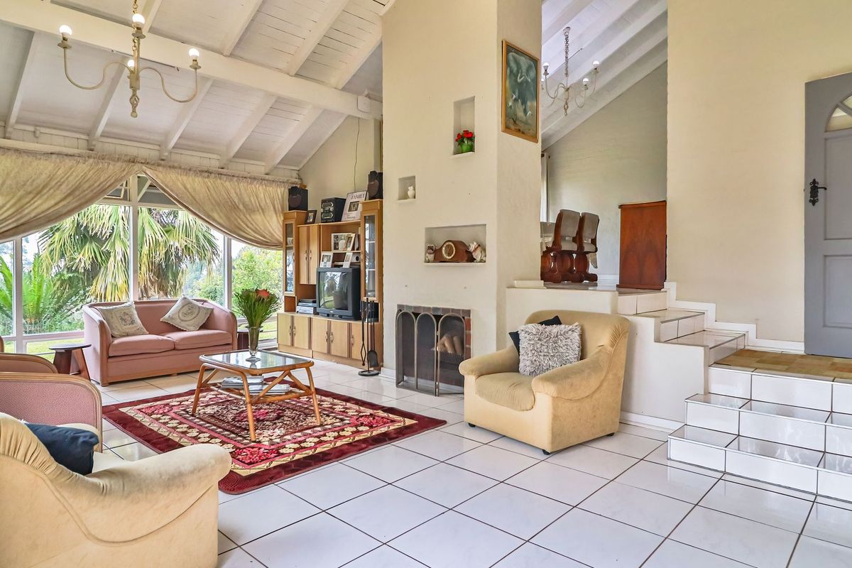 Spacious living room featuring a vaulted ceiling with exposed beams, tiled flooring, and a central fireplace, offering a bright and open atmosphere.