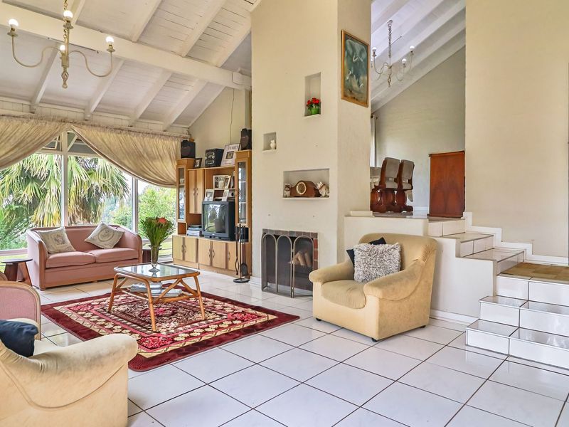 Spacious living room featuring a vaulted ceiling with exposed beams, tiled flooring, and a central fireplace, offering a bright and open atmosphere.