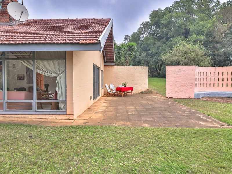Rear view of the house featuring a paved patio, large glass sliding doors, and a unique curved decorative brick wall set within a garden.