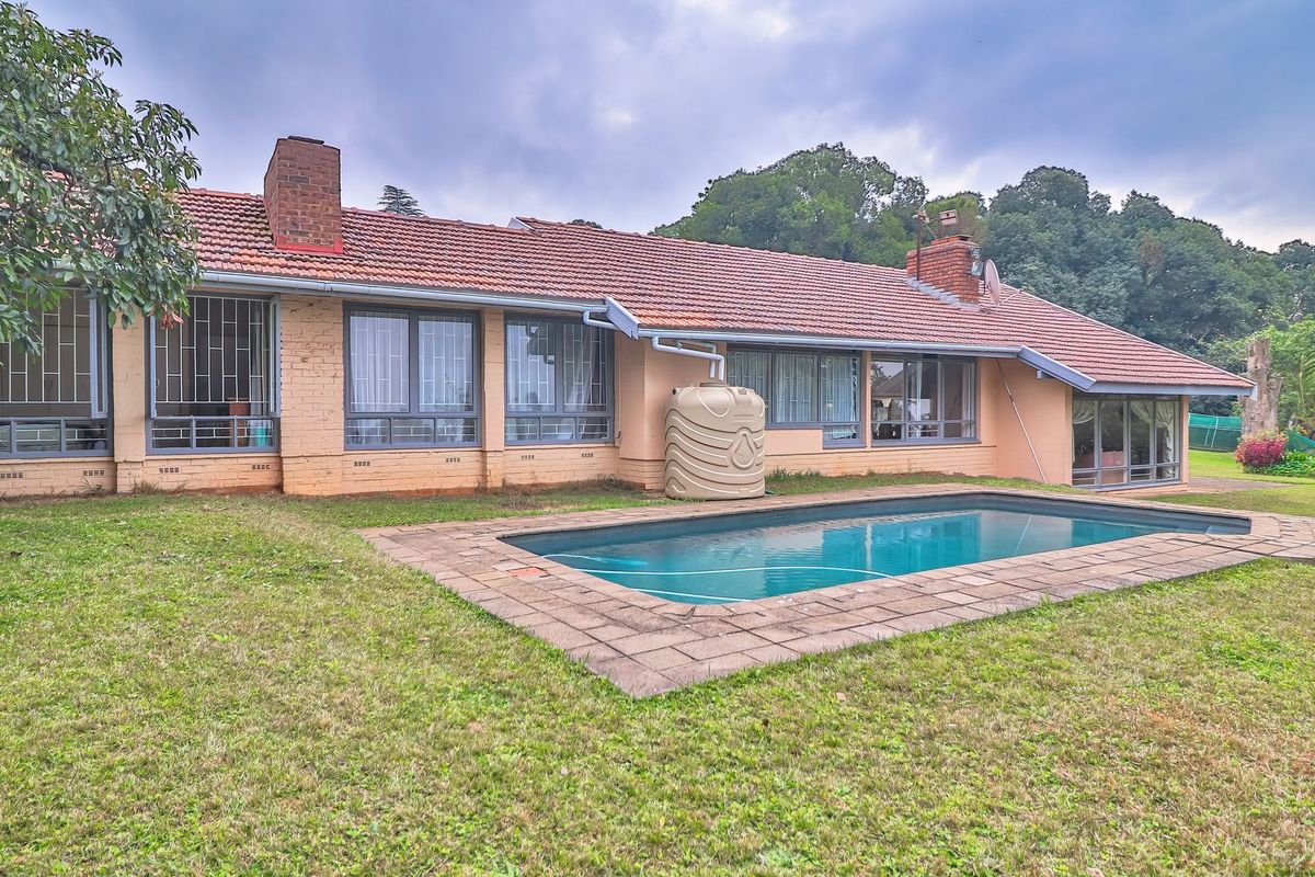 Rear view of the house featuring a swimming pool, brick chimney, tiled roof, and a water storage tank set within a spacious garden.