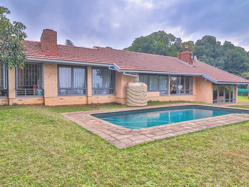 Rear view of the house featuring a swimming pool, brick chimney, tiled roof, and a water storage tank set within a spacious garden.