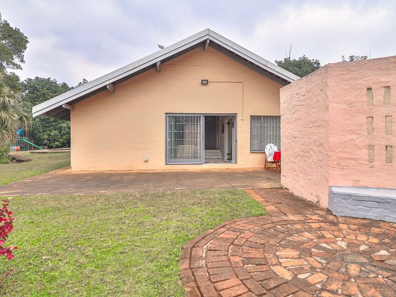 Rear view of the house featuring a paved patio area, brick boundary wall, and access to the interior through security gates.