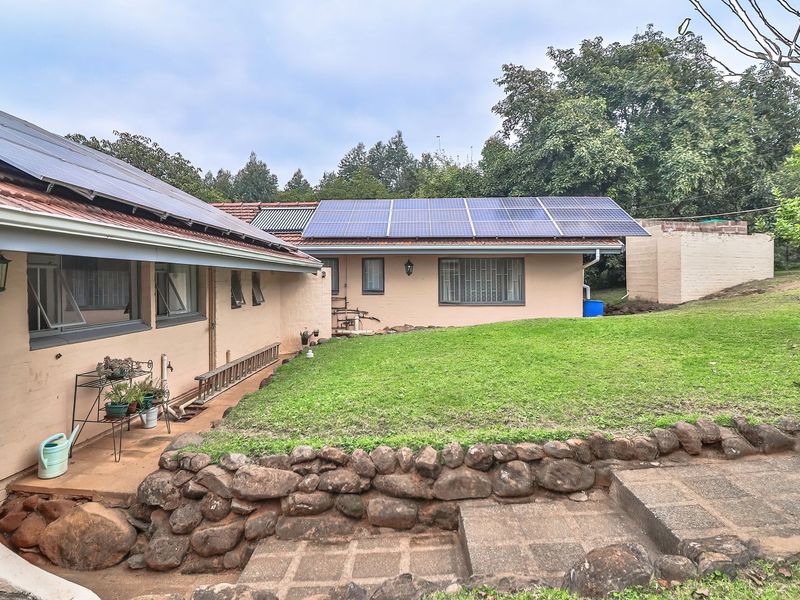 Rear view of the house featuring a landscaped garden, stone retaining wall, concrete steps, and roof-mounted solar panels and geyser system.