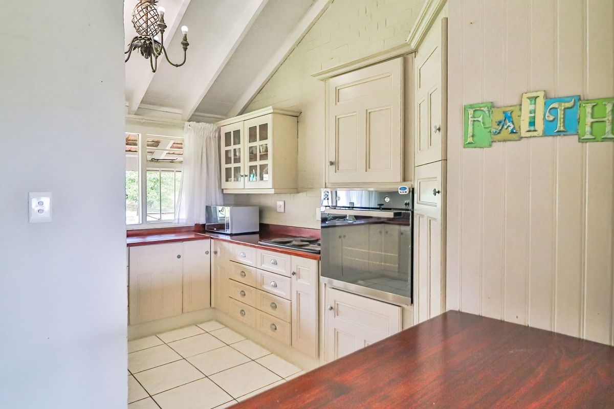 A functional kitchen featuring built-in cabinetry, timber countertops, a built-in oven, and exposed rafters, offering a classic aesthetic with tiled flooring.