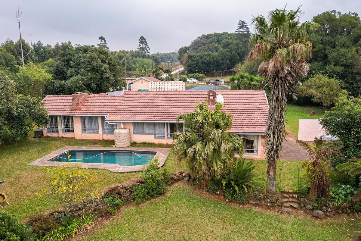 Aerial view of a single-story residential property featuring a swimming pool, tiled roof, and expansive garden area set within a natural landscape.