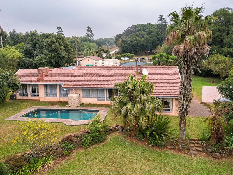 Aerial view of a single-story residential property featuring a swimming pool, tiled roof, and expansive garden area set within a natural landscape.