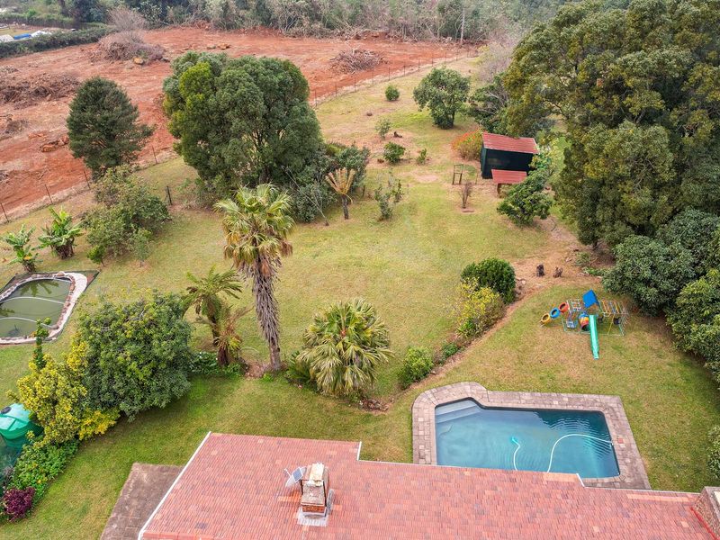 Aerial view of a spacious property featuring a swimming pool, a garden pond, mature trees, and a large landscaped backyard area.