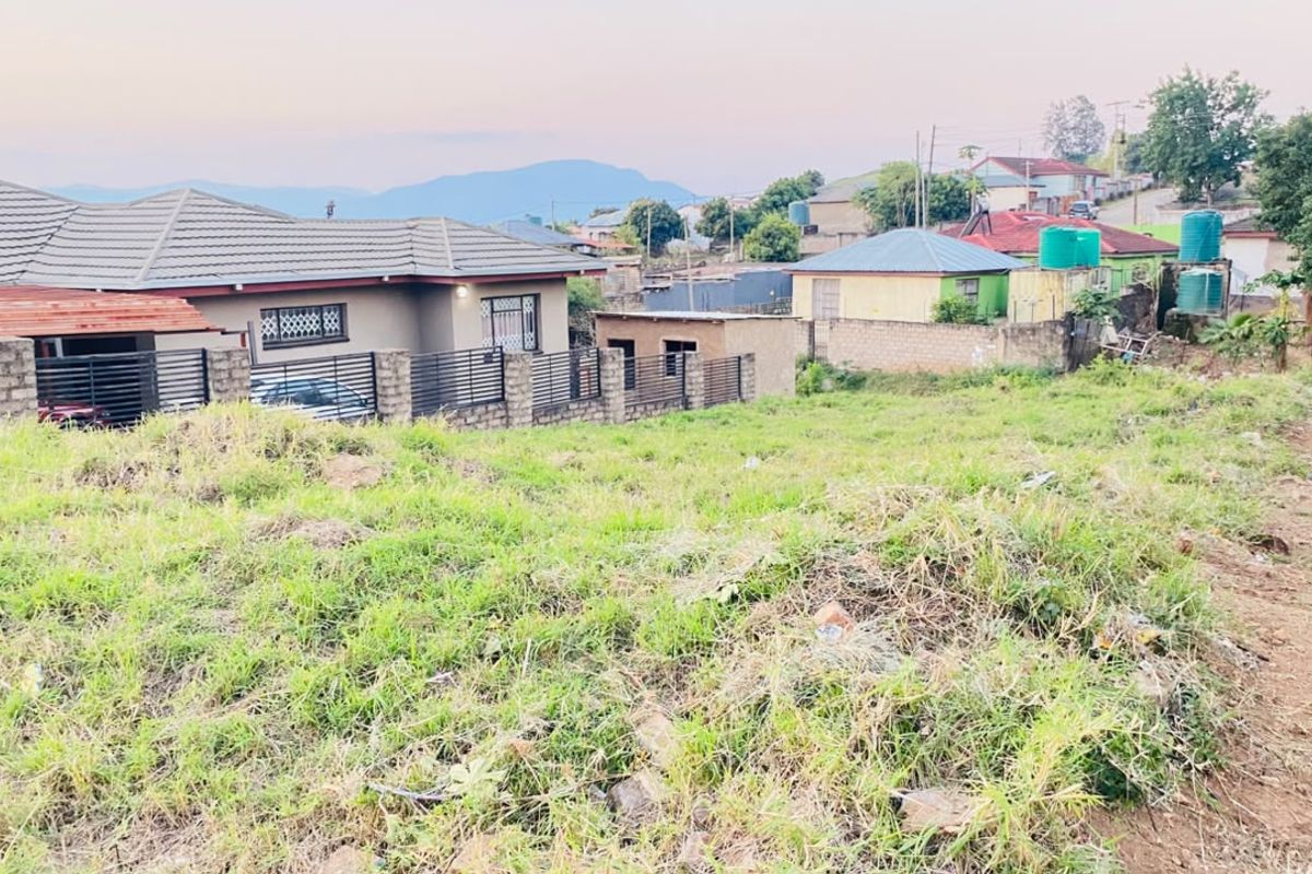 A view of a vacant residential plot featuring grassy terrain, enclosed by boundary walls and fencing, situated within an established neighborhood.