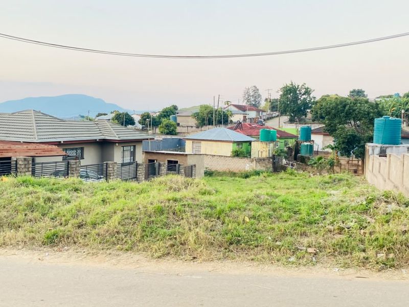 A vacant residential plot situated in a developed neighborhood, featuring a grassed surface and boundary walling.