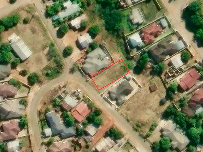 An aerial view of a vacant residential plot situated within an established suburban neighborhood.