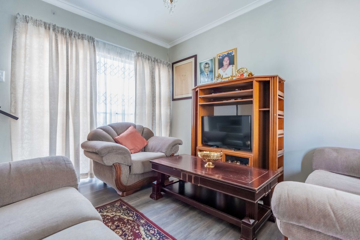 A comfortable living room featuring laminate flooring, coving, and large windows with security gates, providing a functional and well-lit space.