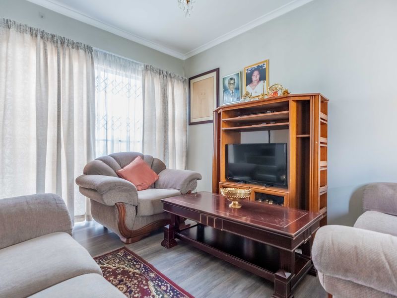 A comfortable living room featuring laminate flooring, coving, and large windows with security gates, providing a functional and well-lit space.