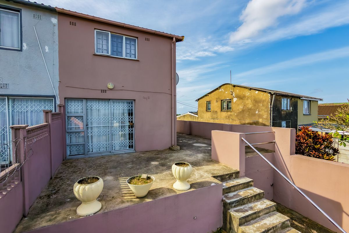 Rear exterior view of the townhouse featuring a concrete patio, staircase with metal handrail, and sliding glass door access.