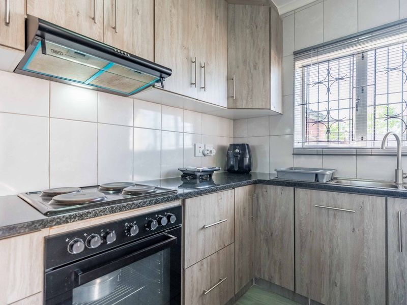 A functional kitchen featuring wood-look cabinetry, granite countertops, a built-in electric stove with extractor fan, and a tiled backsplash.