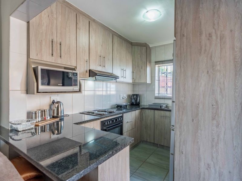 A functional kitchen featuring light wood-grain cabinetry, dark granite countertops, built-in oven, hob, extractor fan, and a built-in microwave.