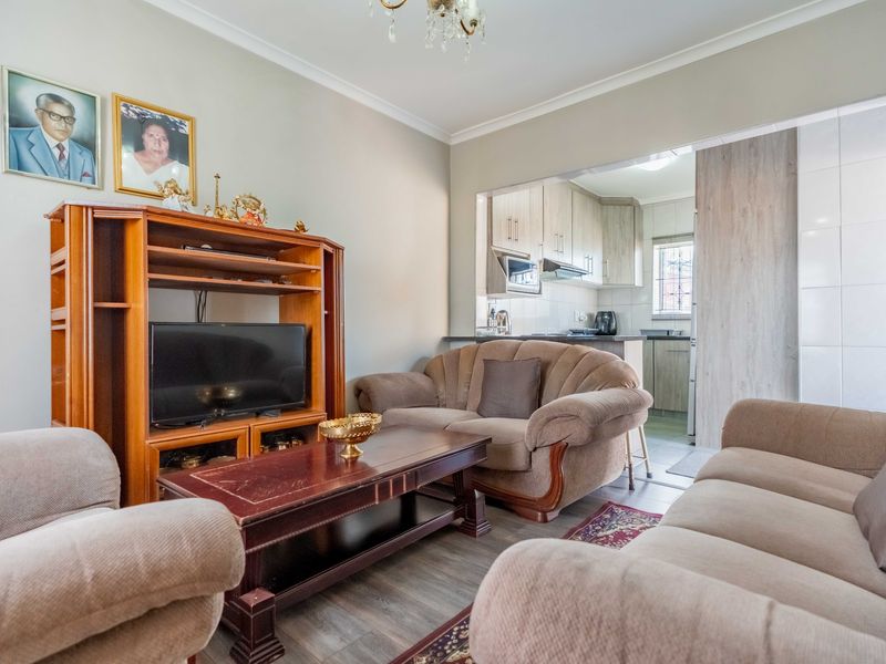 Open plan living area featuring laminate flooring and coving, seamlessly connected to a functional kitchen with built-in cabinetry and appliances.