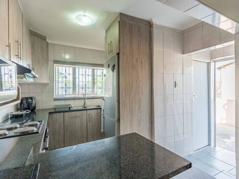 A functional kitchen featuring wood-look cabinetry, granite countertops, an electric hob, and direct access to an outdoor area.