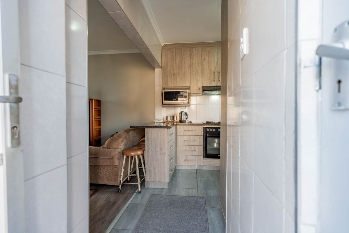 A compact, functional kitchen featuring light wood-finish cabinetry, granite countertops, built-in oven, and an integrated microwave, seamlessly flowing into the adjacent living area.
