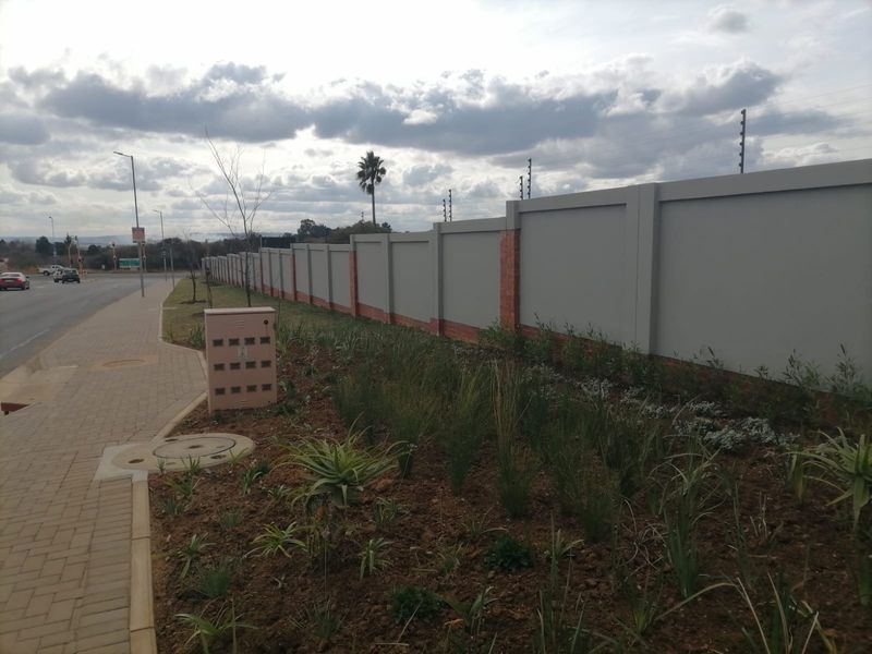 Street view of the property boundary featuring a well-maintained perimeter wall with electric fencing and a paved sidewalk.