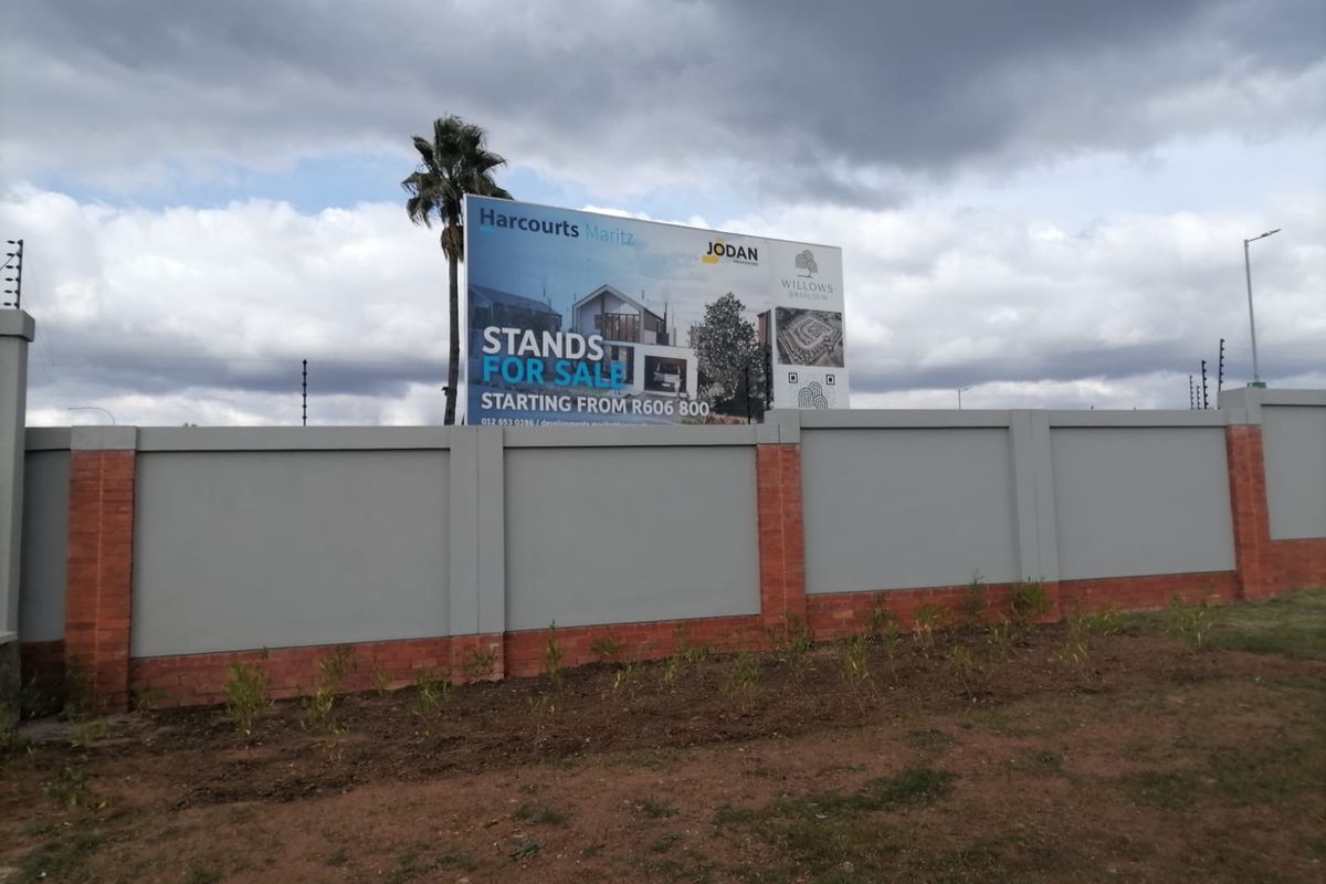 A view of the residential development site featuring a secure perimeter wall with electric fencing and a large promotional billboard.