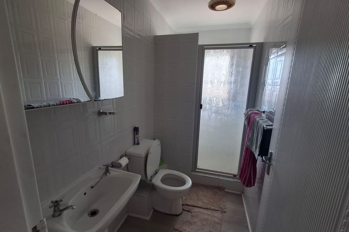 A functional bathroom featuring a pedestal basin, toilet, and a separate shower enclosure with tiled walls and a wall-mounted mirror.