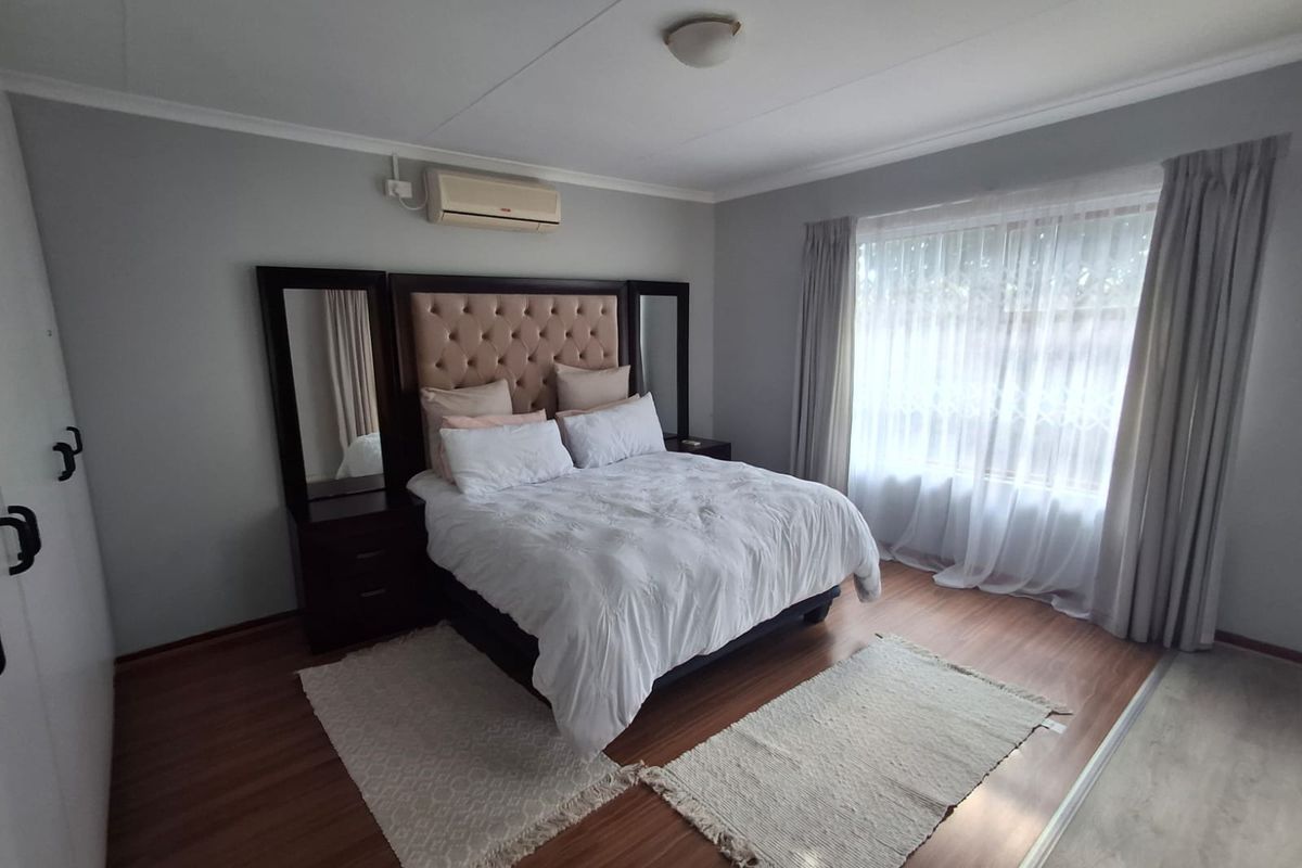 A well-maintained bedroom featuring laminate flooring, built-in cupboards, and a wall-mounted air conditioning unit, offering a comfortable and functional living space.