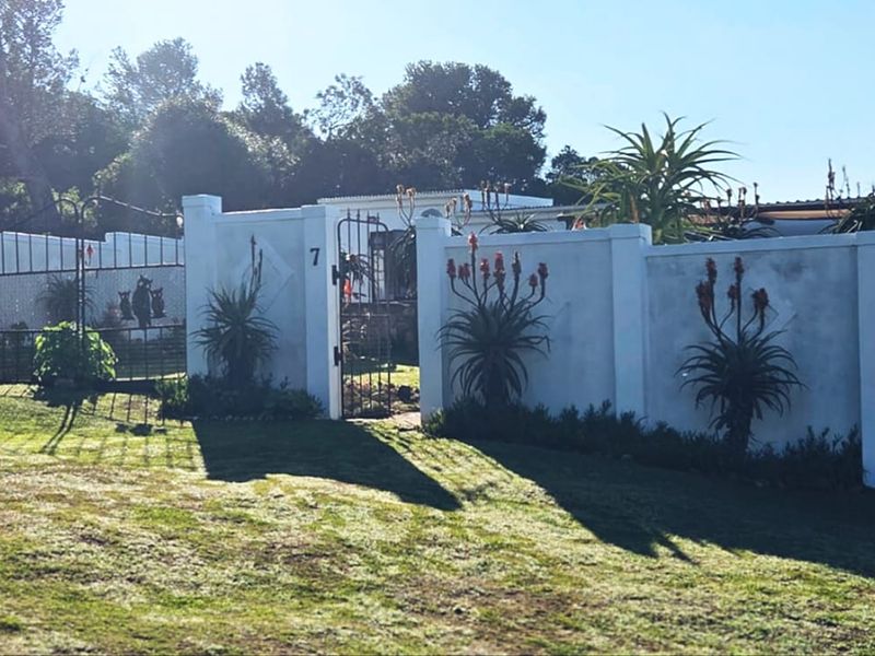 Front view of the property featuring a white perimeter wall with a wrought iron gate entrance and landscaped garden area.