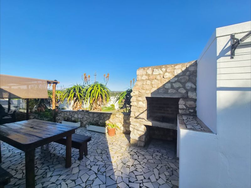 Outdoor patio area featuring a built-in stone braai, stone paving, and a pergola, offering a functional space for outdoor entertaining.