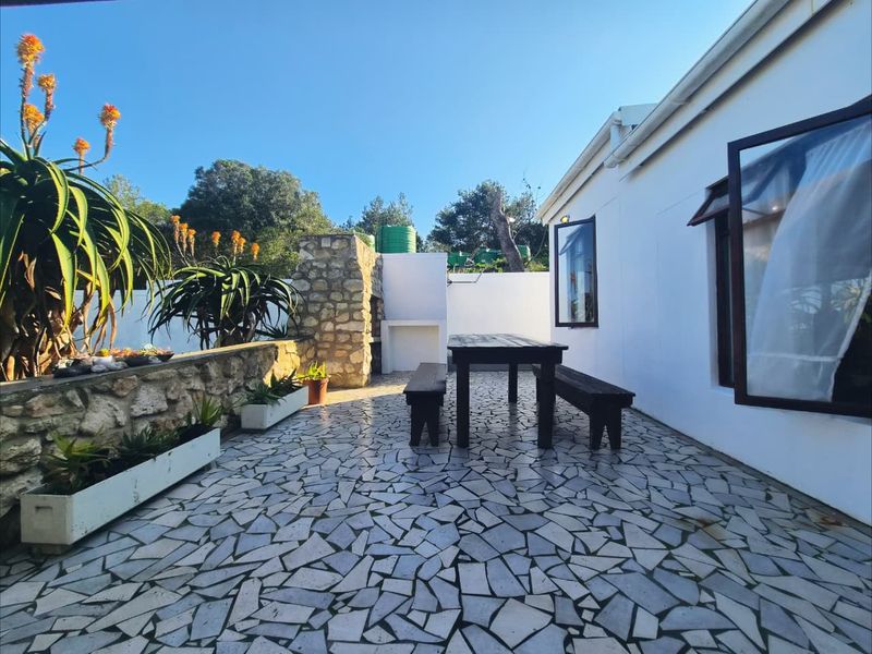 Outdoor patio area featuring crazy paving flooring, a stone-clad built-in braai, and integrated stone retaining walls with built-in planters.
