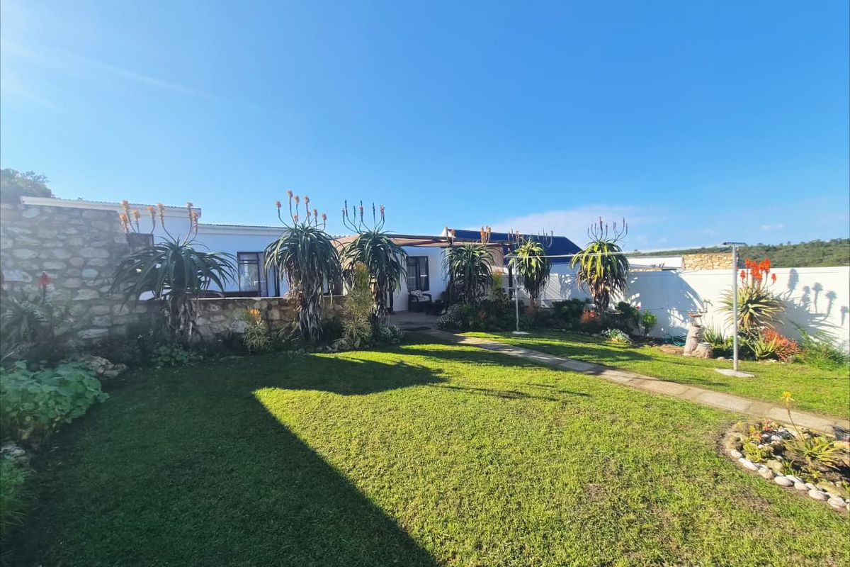 A well-maintained rear garden featuring a stone retaining wall, a paved walkway, and established landscaping with a lawn area.