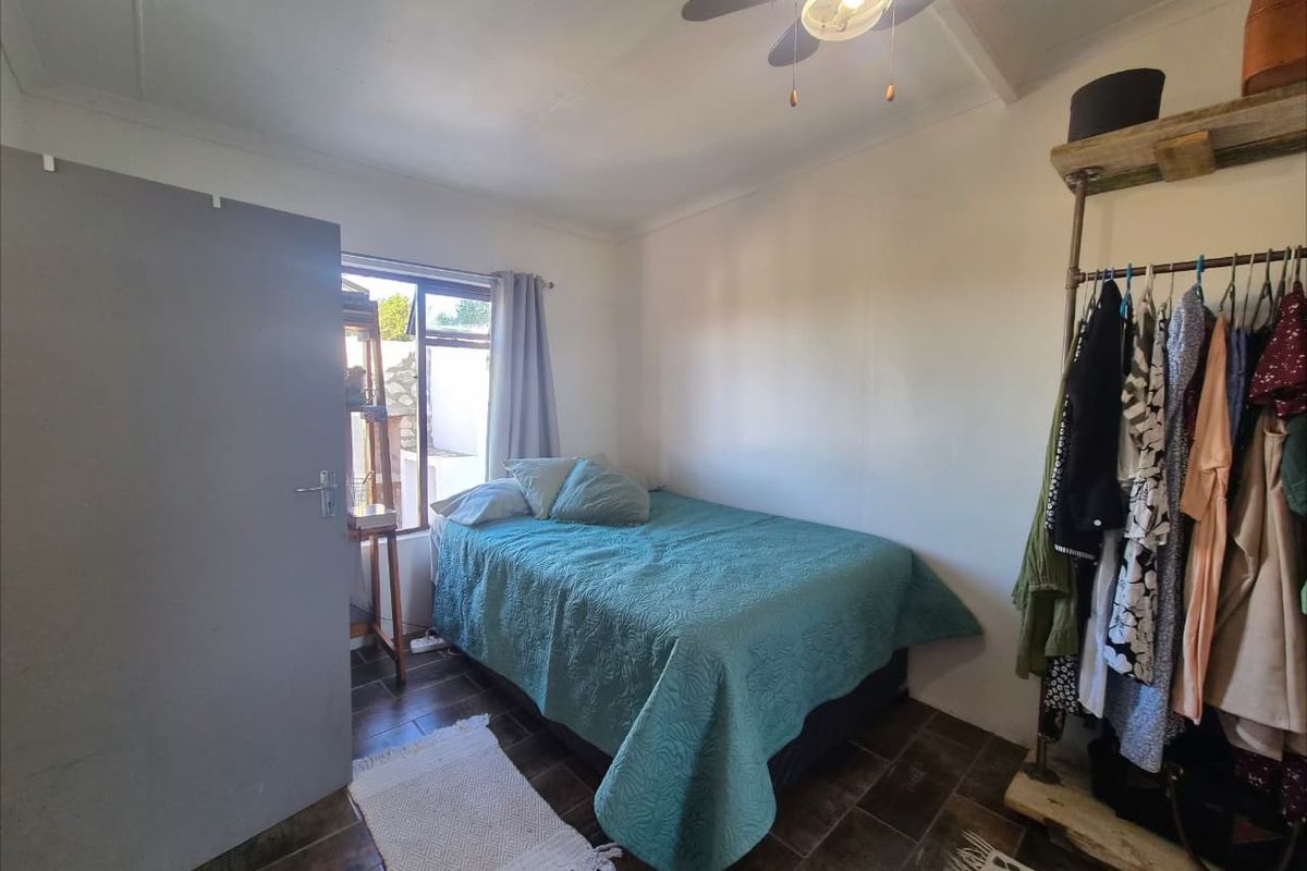 A compact bedroom featuring tiled flooring, a ceiling fan, and a window, providing a functional and well-lit sleeping space.