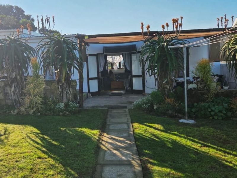 Rear view of the property featuring a landscaped garden, stone retaining wall, paved pathway, and a covered patio area with timber pergola structure.