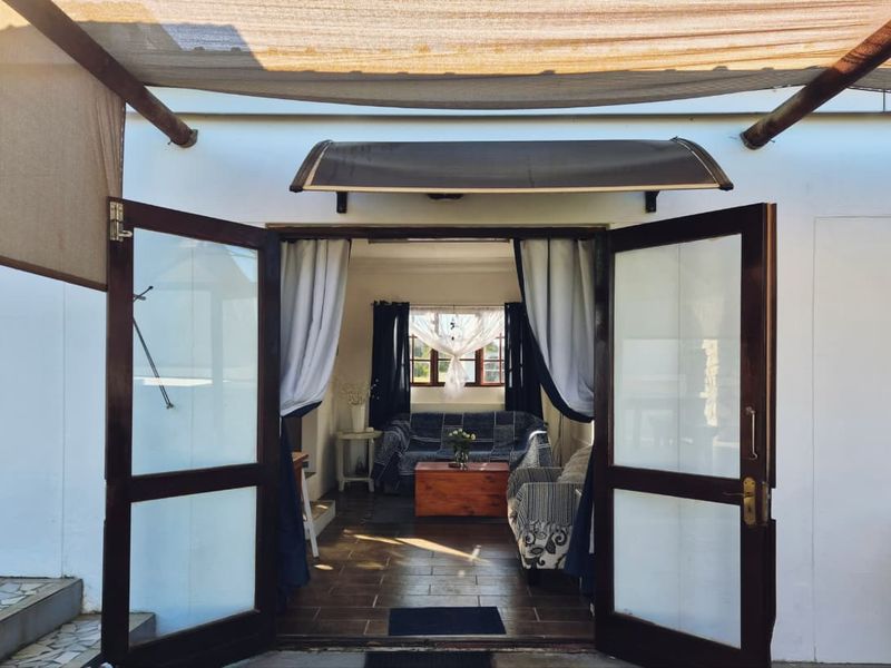 A covered patio area featuring tiled flooring and timber-framed glass double doors leading into the interior living space.