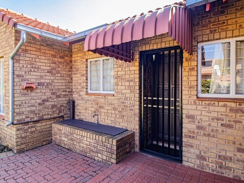 A well-maintained rear exterior area featuring face brick walls, a paved patio, a built-in brick planter, and secure access via a metal security gate.
