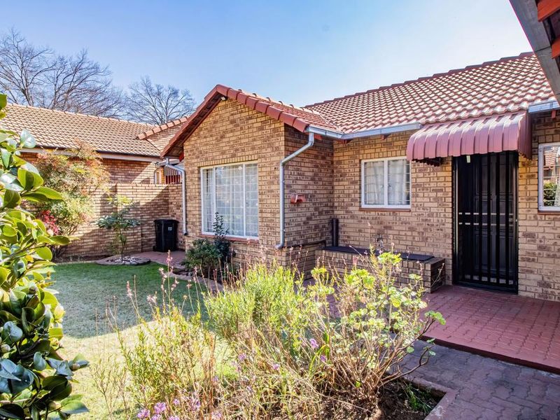 A well-maintained rear exterior view featuring a face brick facade, tiled roof, paved patio area, and a small private garden.
