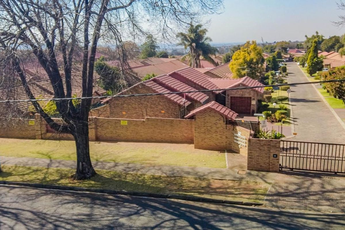 Aerial view of a residential complex featuring brick-walled properties with tiled roofs, secure gated access, and established street landscaping.