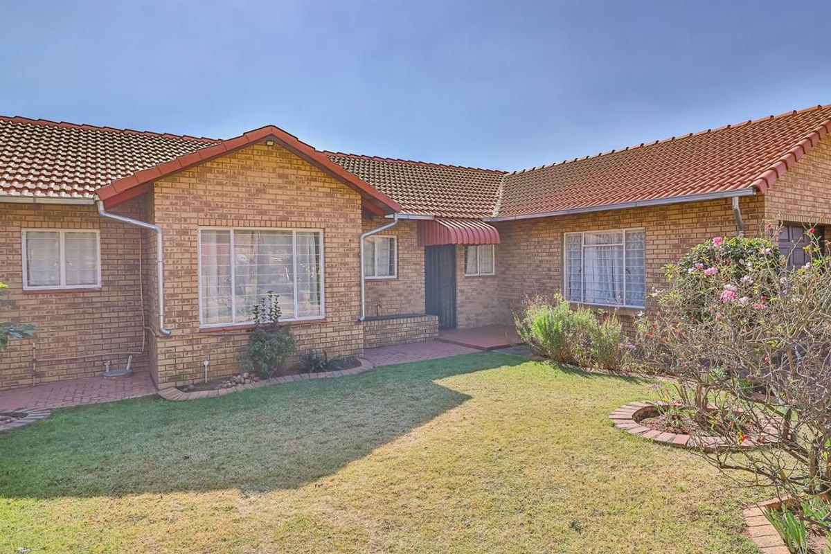 A rear view of a face brick house featuring a tiled roof, metal window frames, and a paved walkway leading to the entrance.