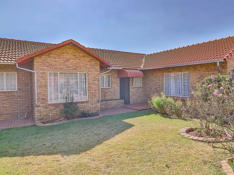 A rear view of a face brick house featuring a tiled roof, metal window frames, and a paved walkway leading to the entrance.