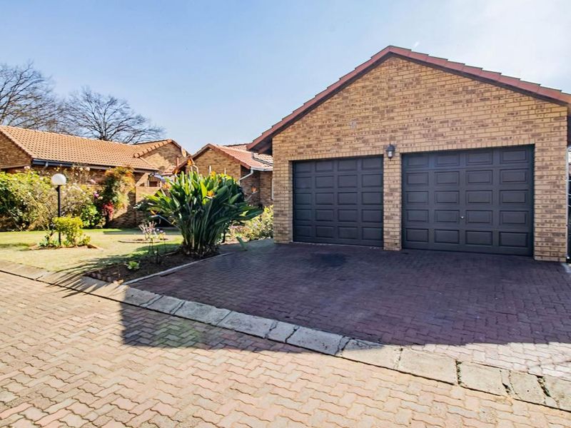 Front view of a residential property featuring a double garage with dark doors, brick paving, and a well-maintained facebrick exterior.