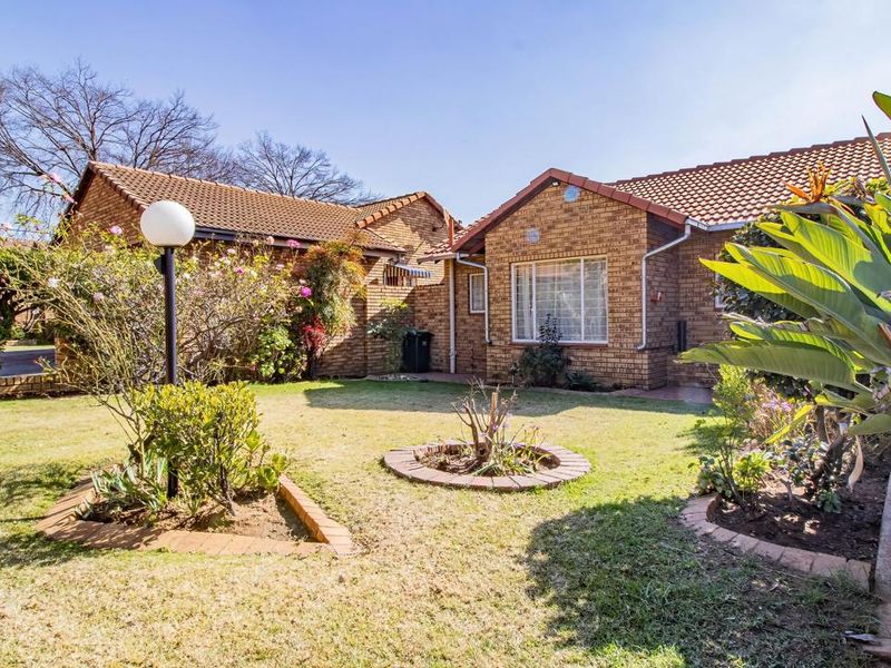 A well-maintained rear garden featuring a face brick facade, tiled roof, and established landscaped garden beds with a paved walkway.