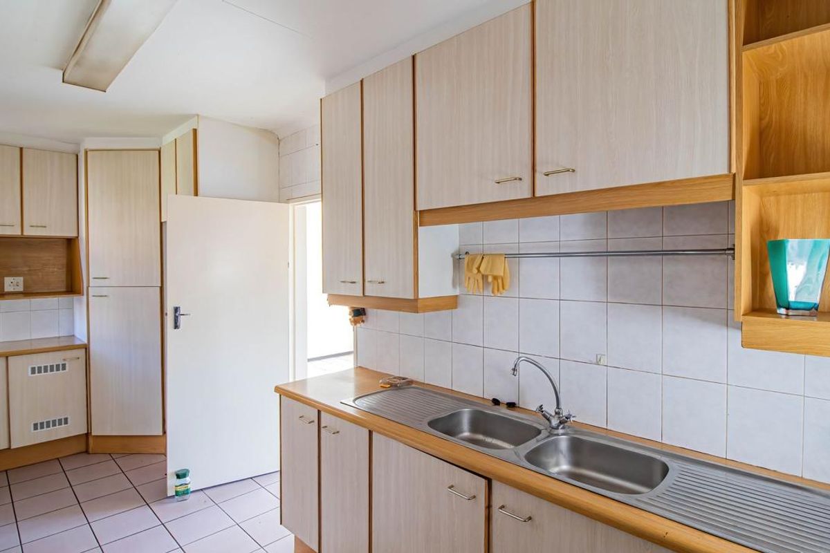 A functional kitchen featuring light wood-look laminate cabinetry, a double stainless steel sink, and tiled splashbacks, offering a clean canvas for potential modern updates.