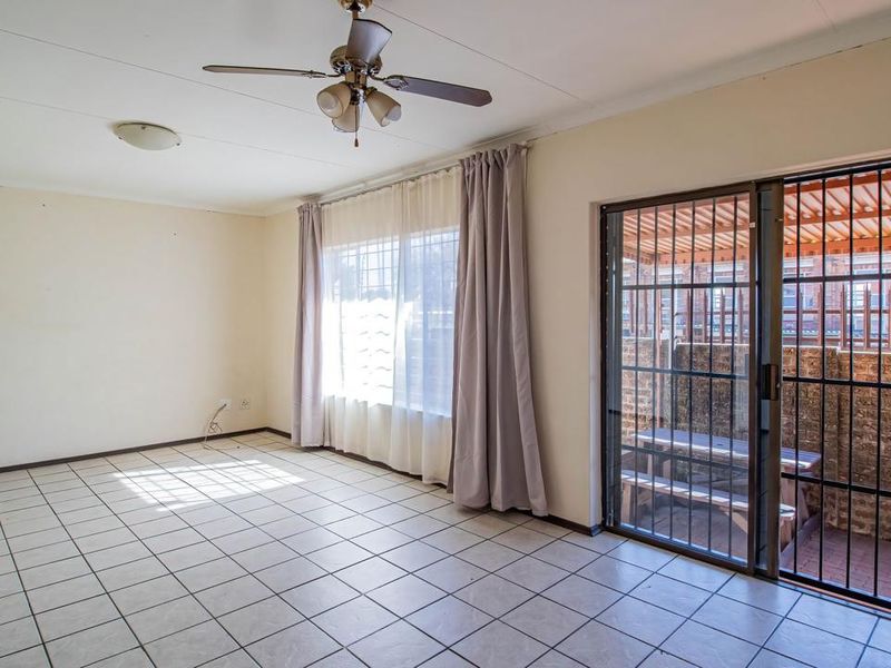 Spacious living area featuring neutral tiled flooring, a ceiling fan, and a sliding glass door with security gate leading to an outdoor patio.