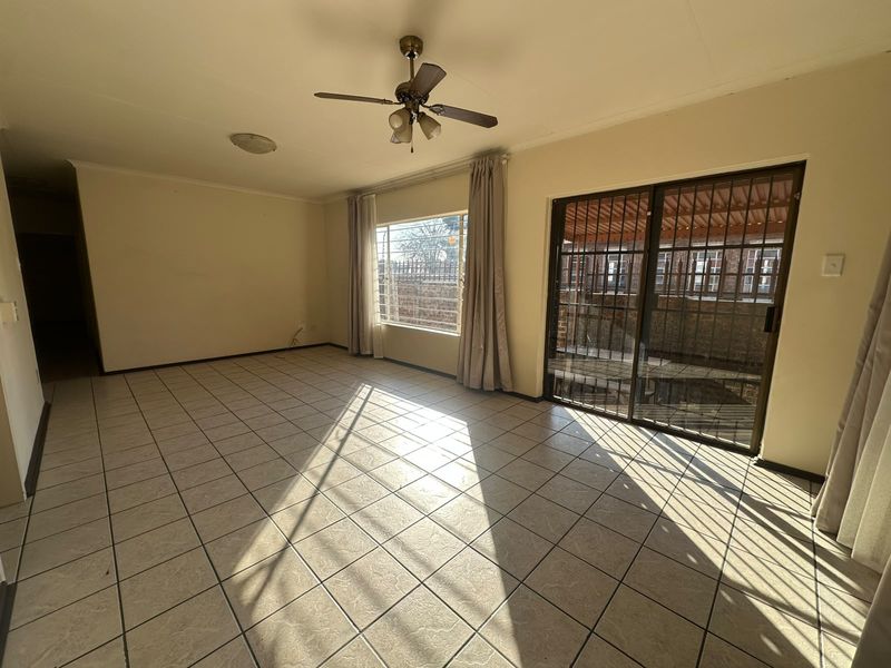 Spacious living area featuring neutral tiled flooring, a ceiling fan, and large windows with security bars, providing access to the outdoor area.